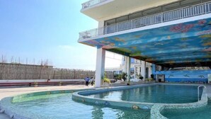 A swimming pool with a mural on the ceiling, a covered area, and a wooden fence in the background. - PGC Chennai Resort & Club By SSS (Ponneri)