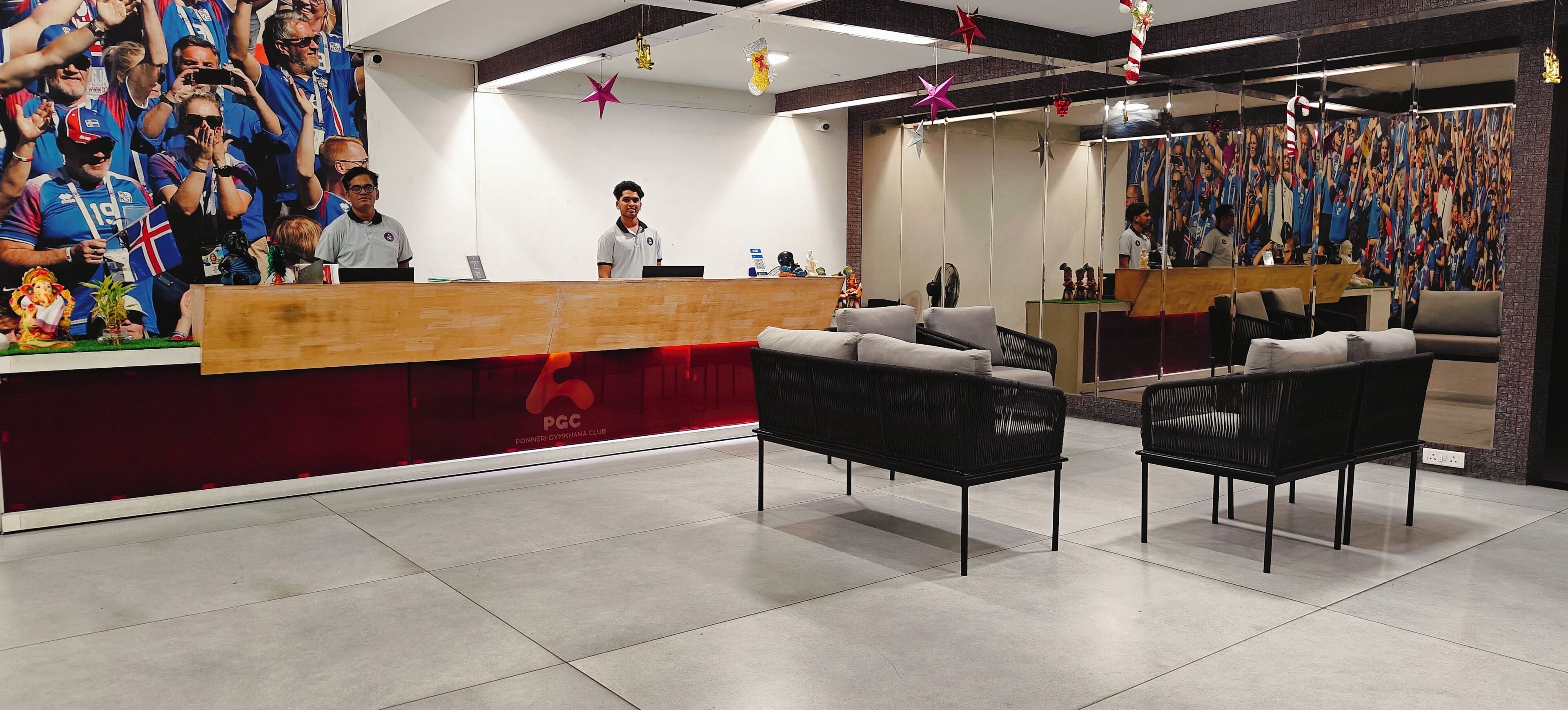 A reception area with a wooden counter, black chairs, and a large mirror reflecting a crowd.