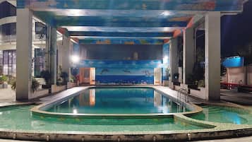 Uma piscina com um mural de golfinhos, cercada por um edifício com teto azul e vista para o céu.