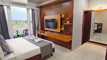 A hotel room with a bed, a TV, a wooden dresser, and a large window with curtains.
