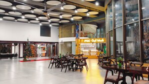 A spacious indoor area with multiple seating arrangements, a Christmas tree, and a large window with a crowd reflection. - PGC Chennai Resort & Club By SSS (Ponneri)