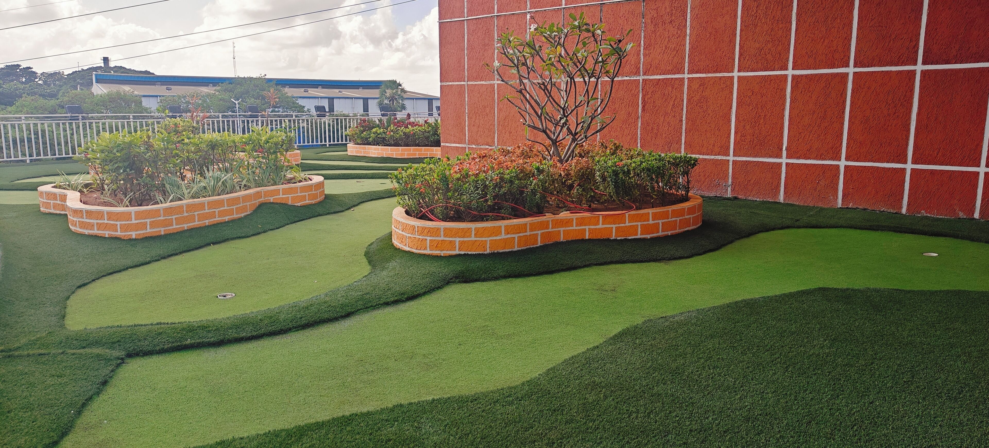 A landscaped outdoor area with artificial grass, brick planters, and a red wall.
