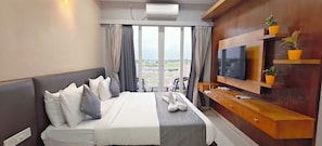 Habitación de hotel con cama, televisor, aparador de madera y plantas en macetas.