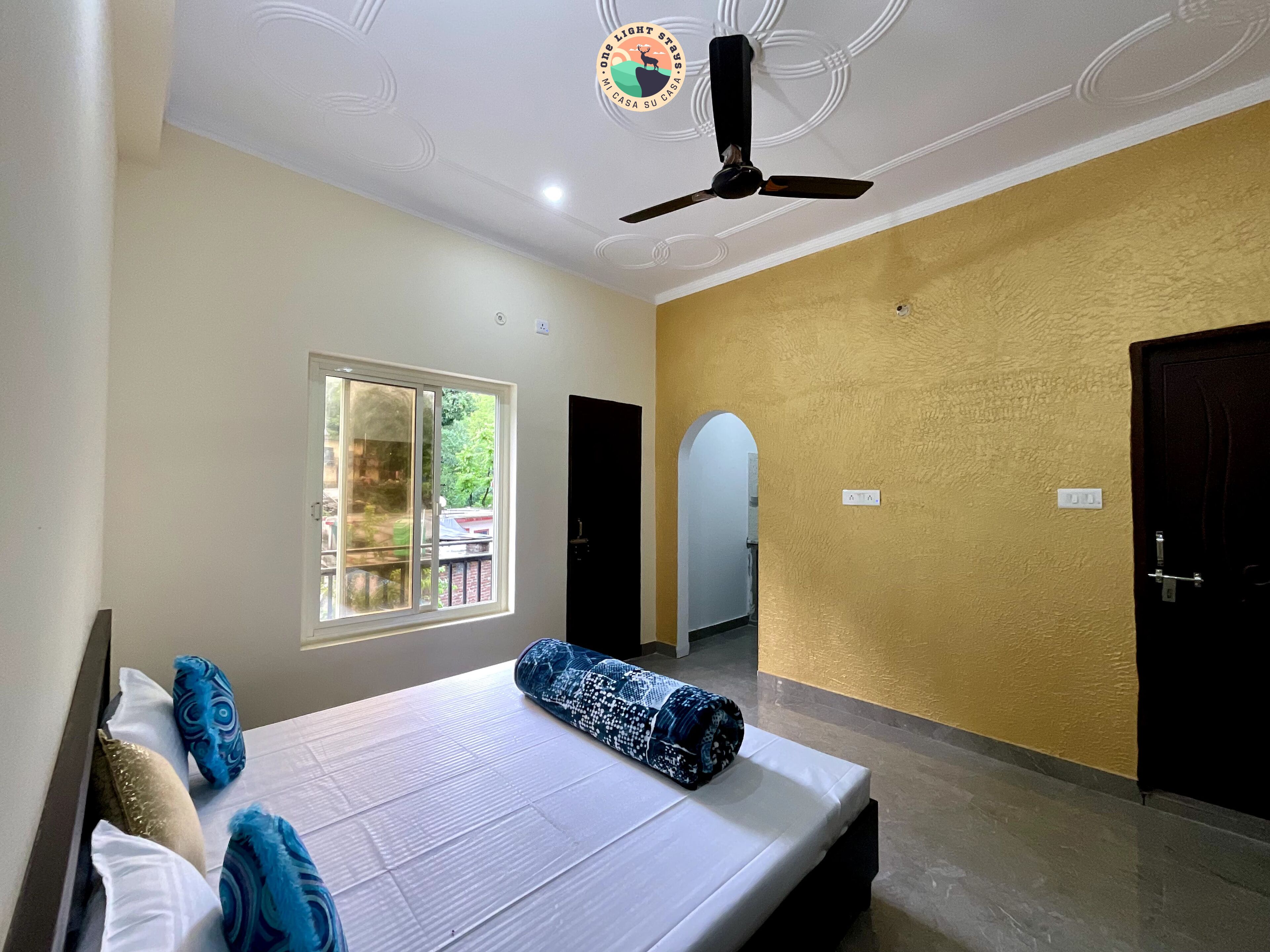 Una habitación de hotel con cama, ventilador de techo, ventana y puerta.