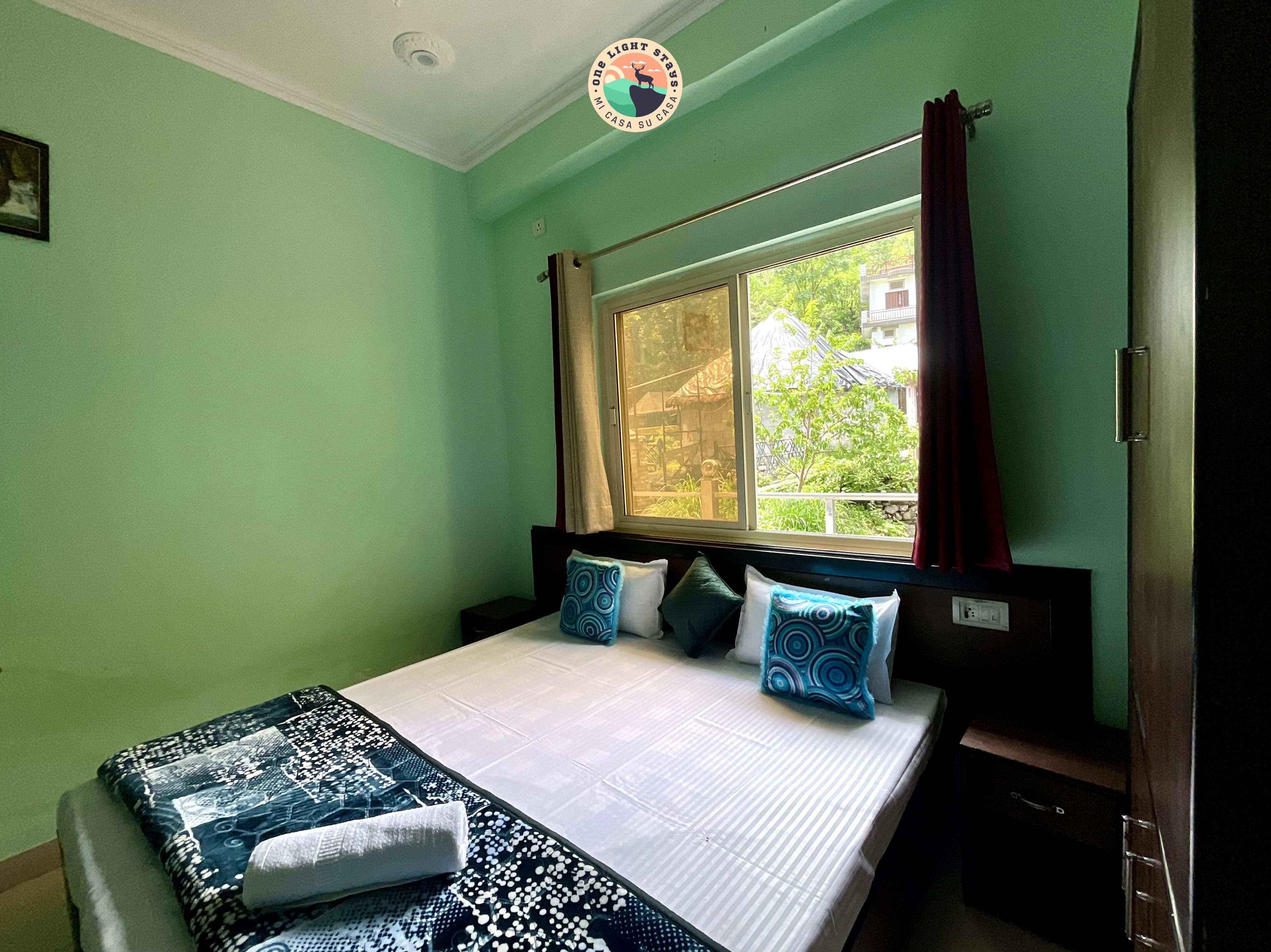 A room with a bed, a window with curtains, and a view of greenery outside.