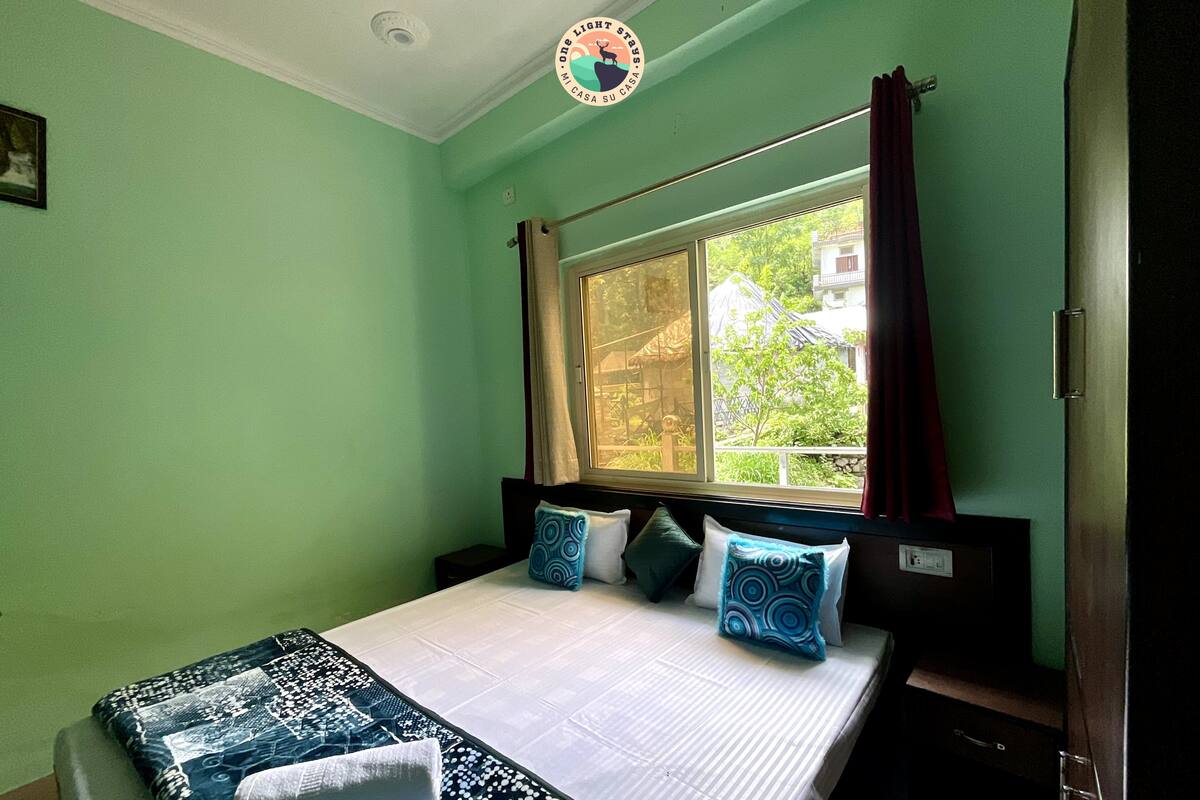 Ein Zimmer mit einem Bett, einem Vorhangfenster und Blick auf Grünfläche.