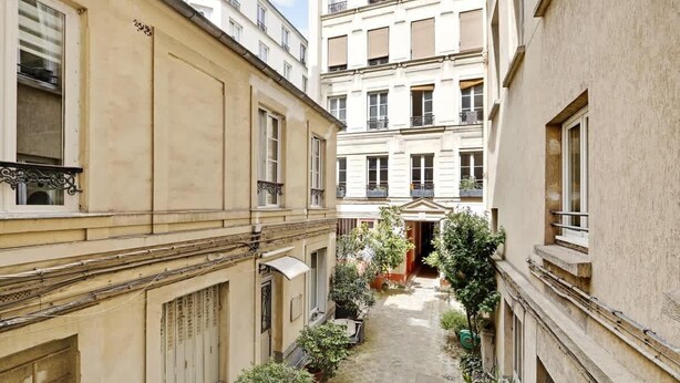 Une ruelle étroite entre deux immeubles, avec des balcons et des plantes en pot.