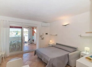 A bedroom with a bed, a bedside table, a chair, and a view through a sliding glass door to an outdoor area with a table and chairs. - Studio St. Teresa (Santa Teresa Gallura)