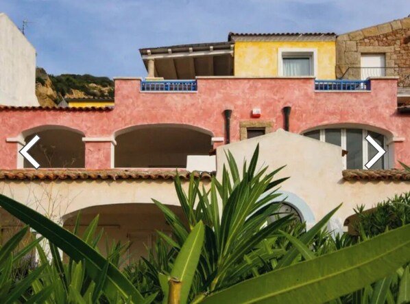 Un bâtiment à la façade rose, doté de nombreuses arcades et d’un balcon avec des balustrades bleues.