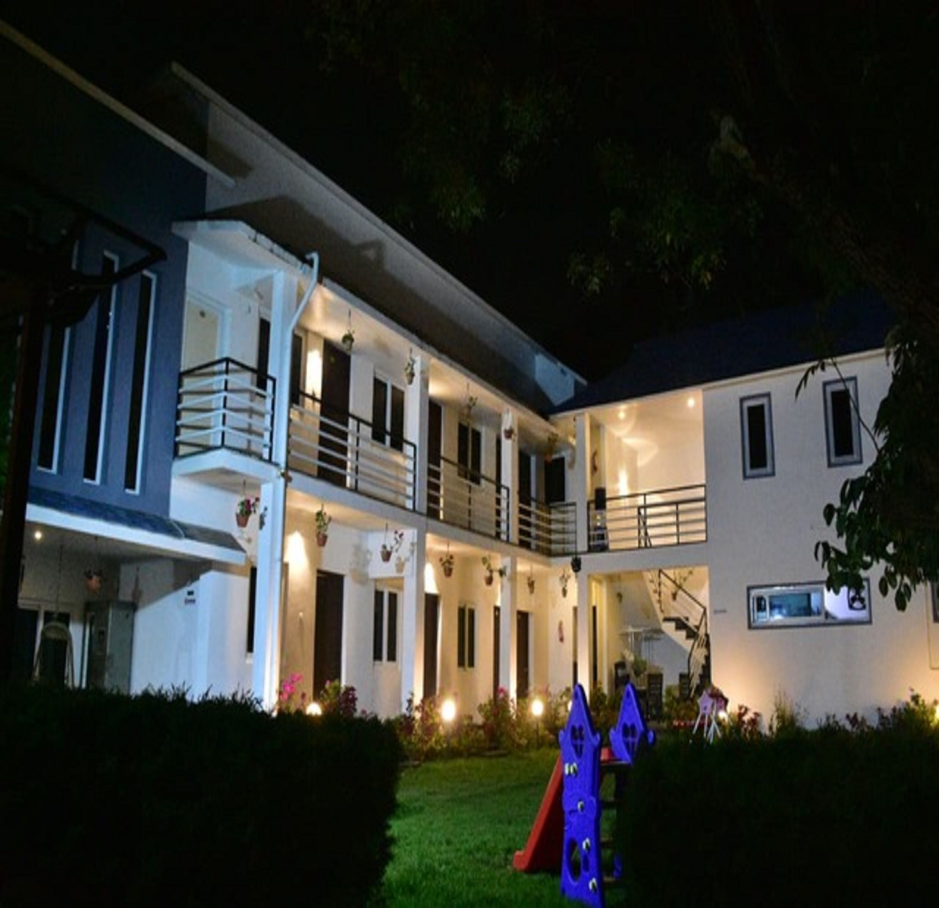 A two-story building with a balcony on the upper floor, a staircase, and a small garden area with a play structure.