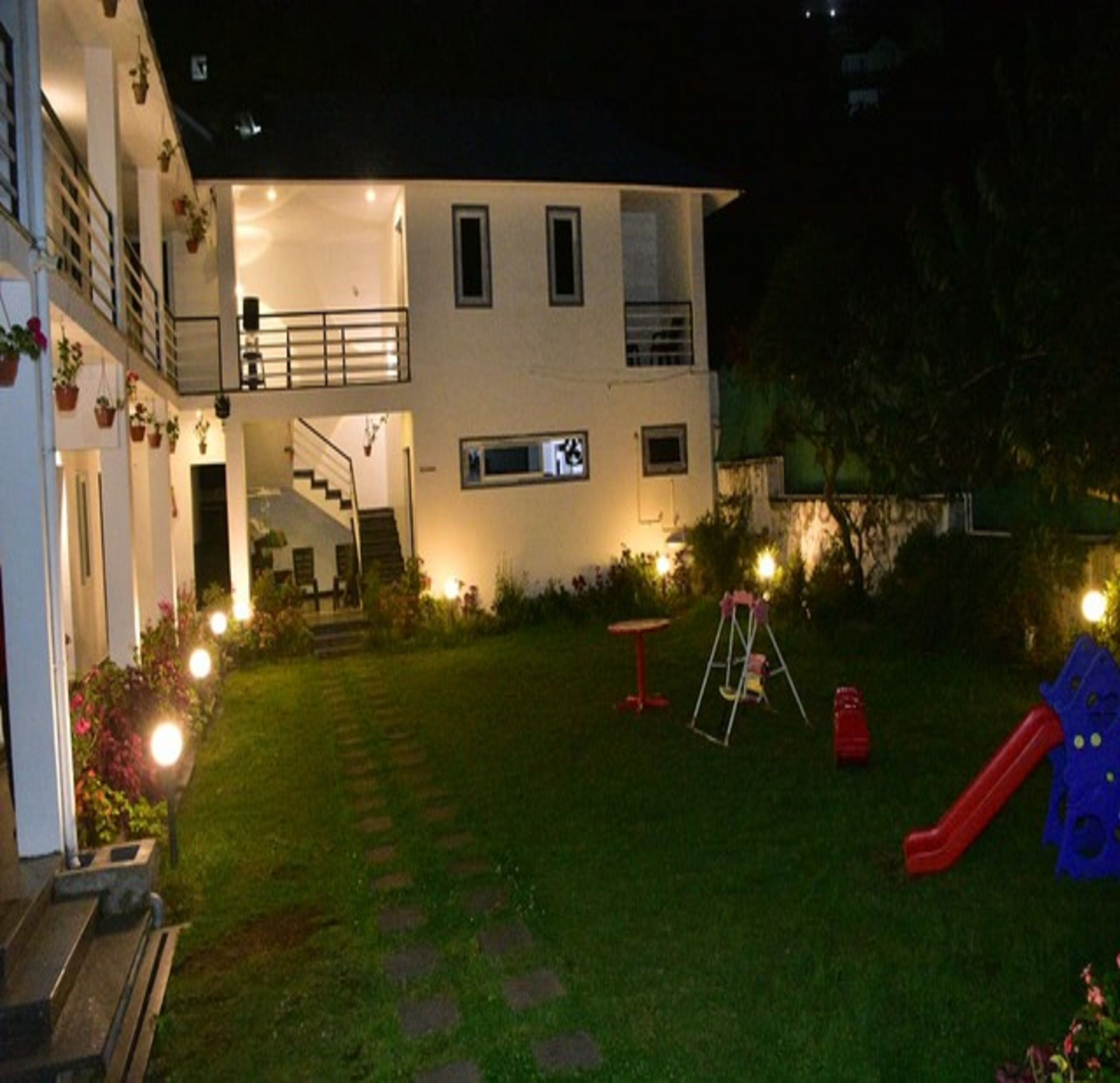 A two-story house with a visible staircase leading to the upper floor. There is a small garden area with a swing set and a slide.