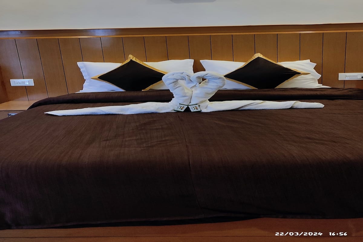 Un lit bien fait, recouvert d’une couverture marron, avec deux oreillers noirs à bordure dorée et une serviette blanche disposée de manière décorative.