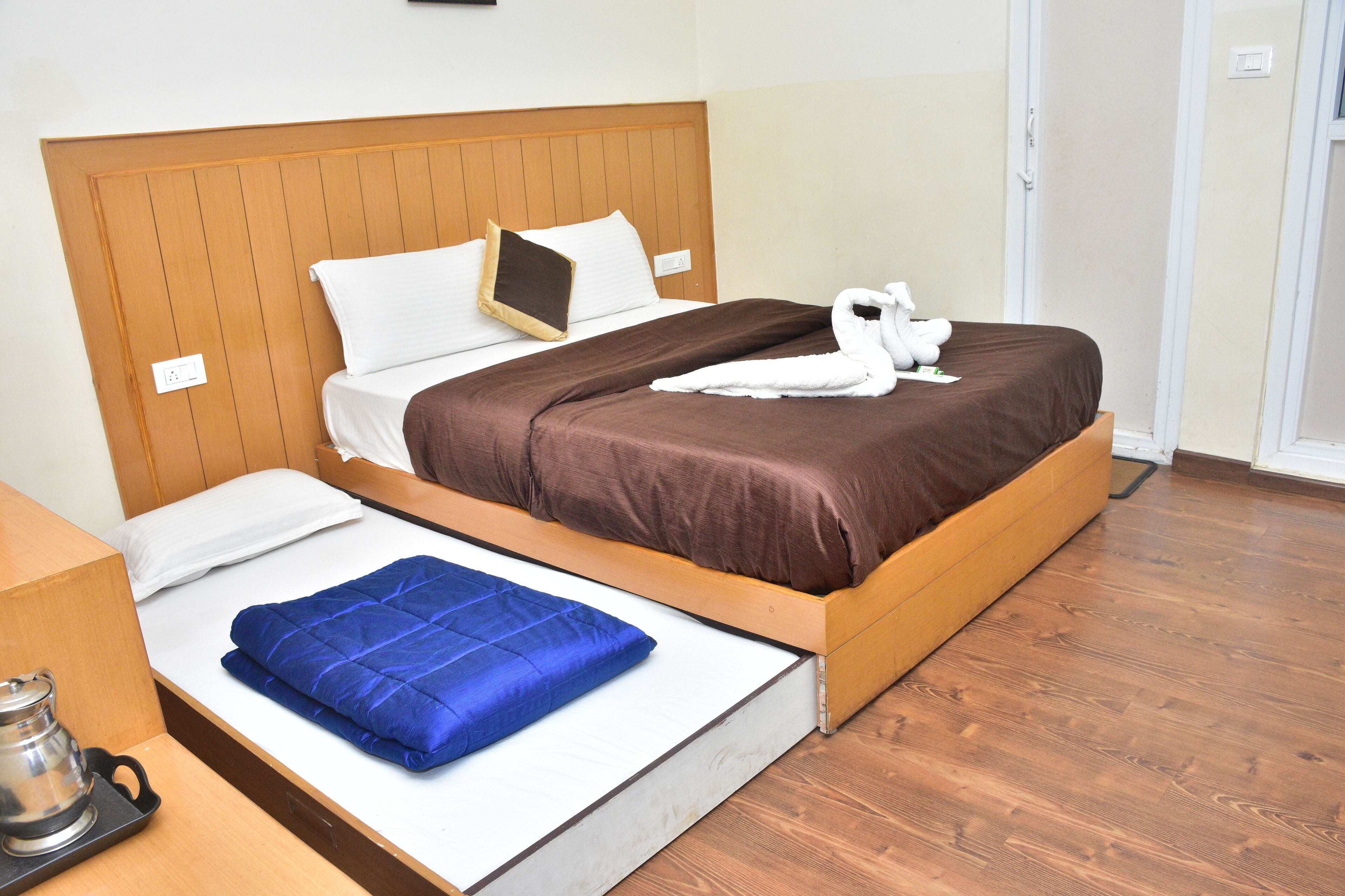 A hotel room with a bed, a blue blanket, a white towel, and a wooden headboard.