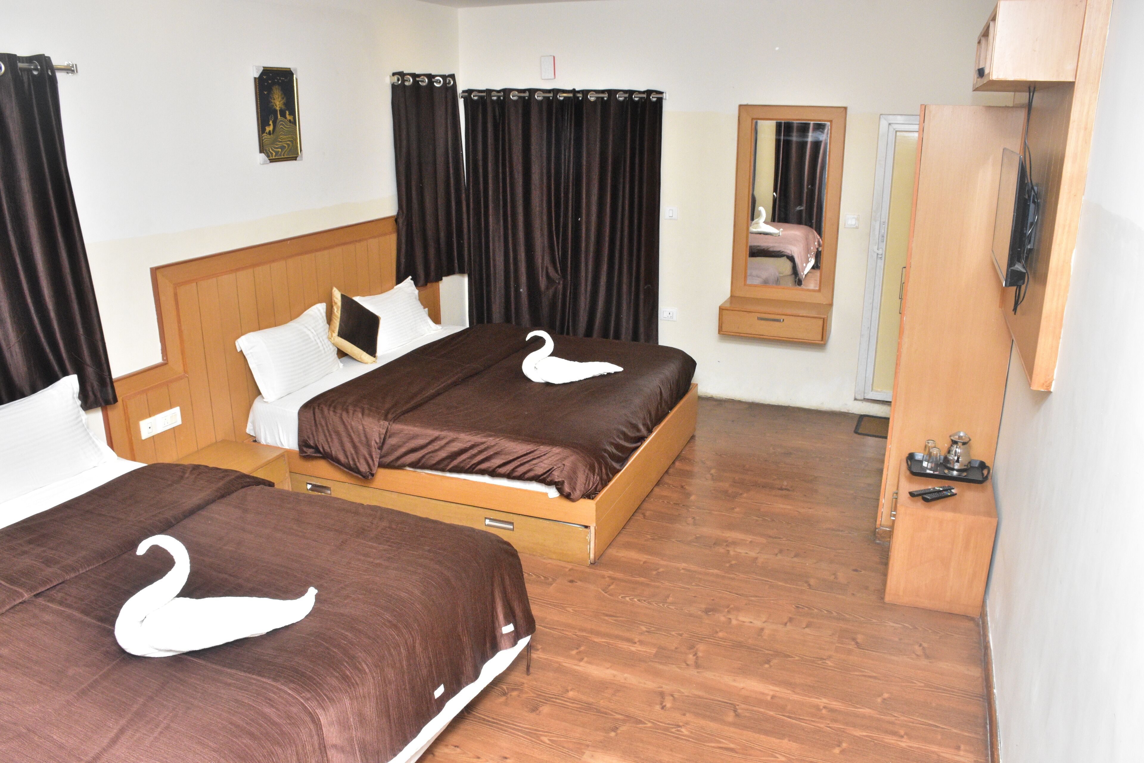 Une chambre d’hôtel avec deux lits, des têtes de lit en bois, des rideaux foncés, un miroir, une armoire en bois et un téléviseur à écran plat.