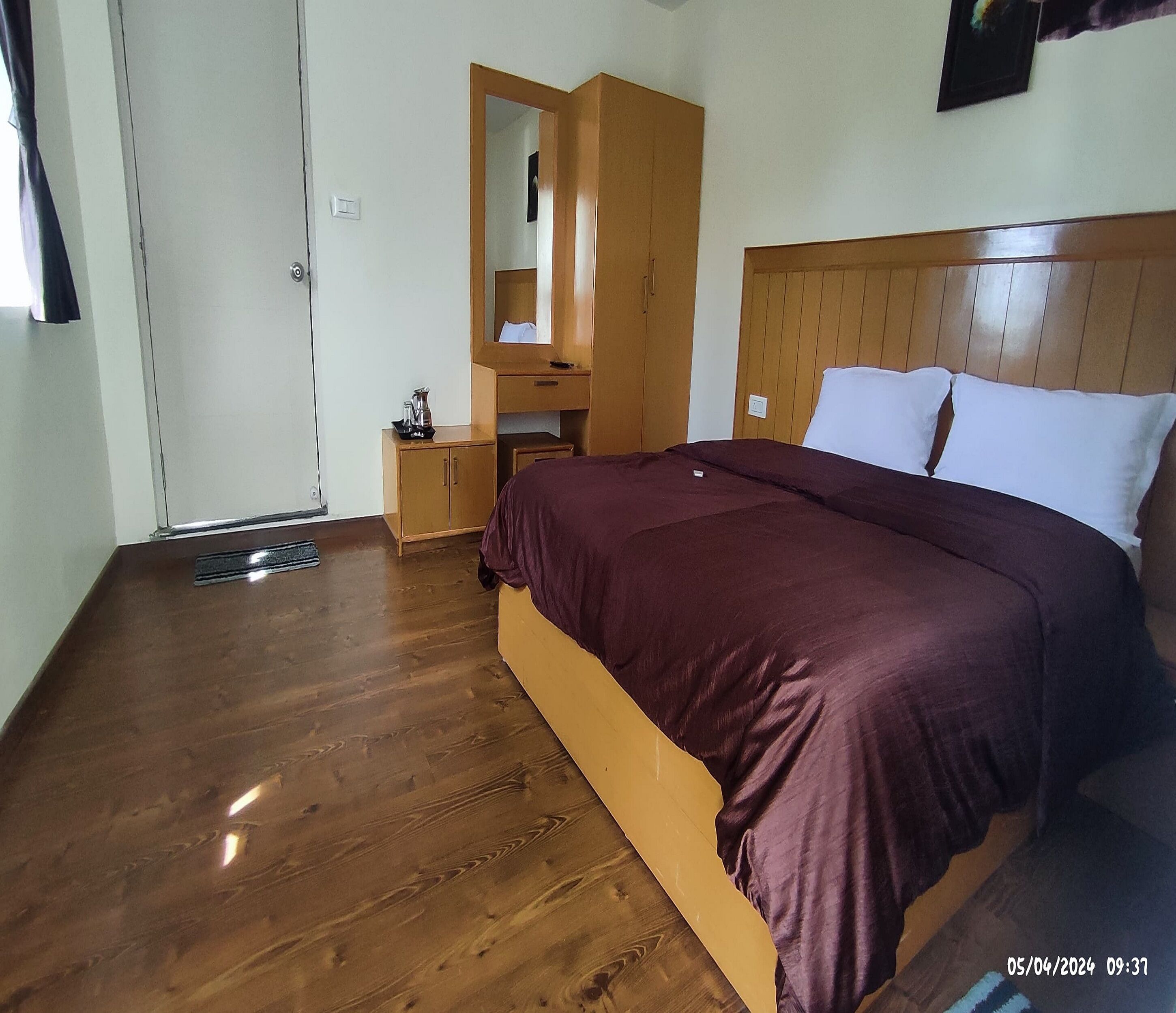 Een slaapkamer met een houten vloer, een bed met hoofdeinde, een nachtkastje, een kledingkast en een spiegel.
