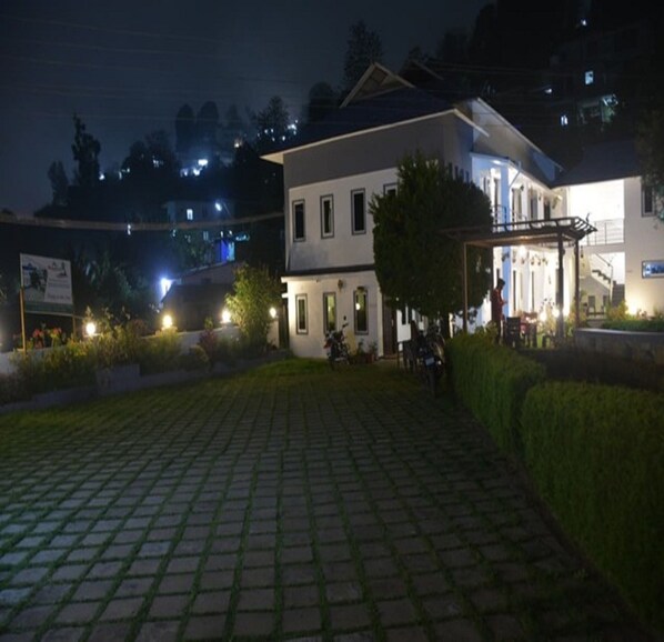 A two-story building with a paved courtyard, a covered outdoor seating area, and a small garden.