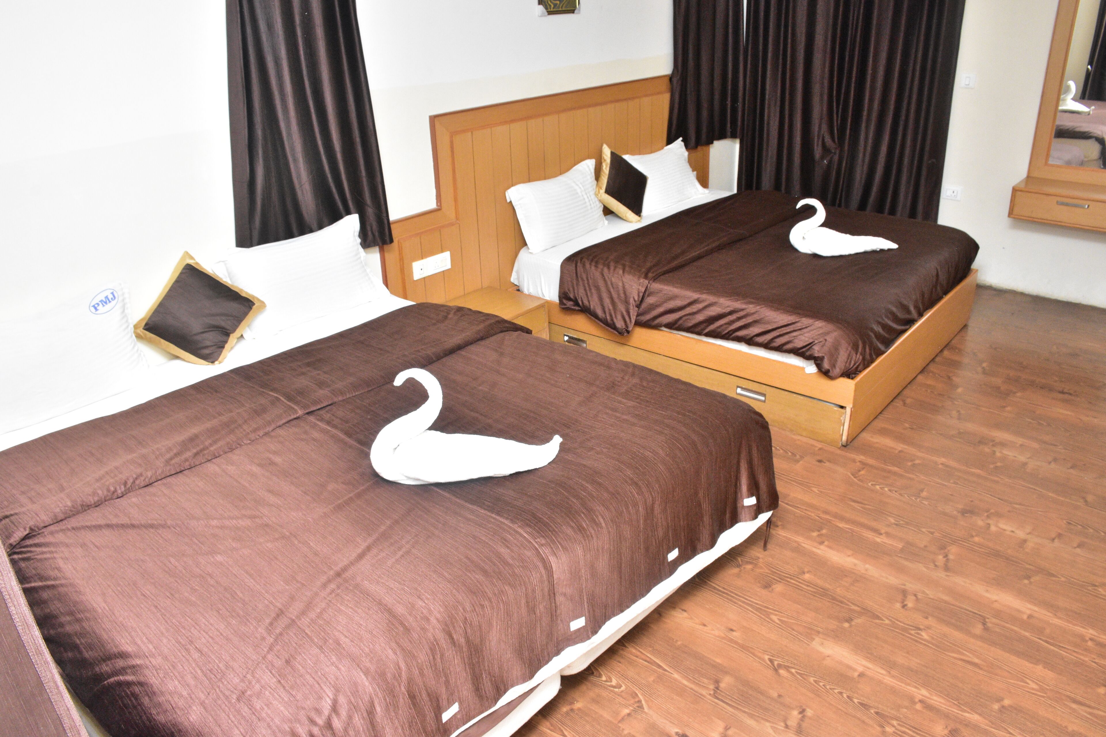 Dos camas individuales con ropa de cama marrón y adornos de cisnes blancos, cabeceros de madera y suelo de madera.