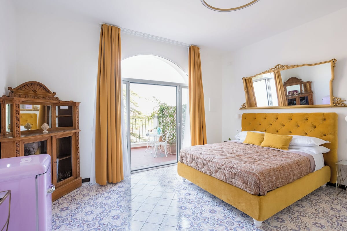 A bedroom with a bed, a dresser, a mirror, and a view to the outside.