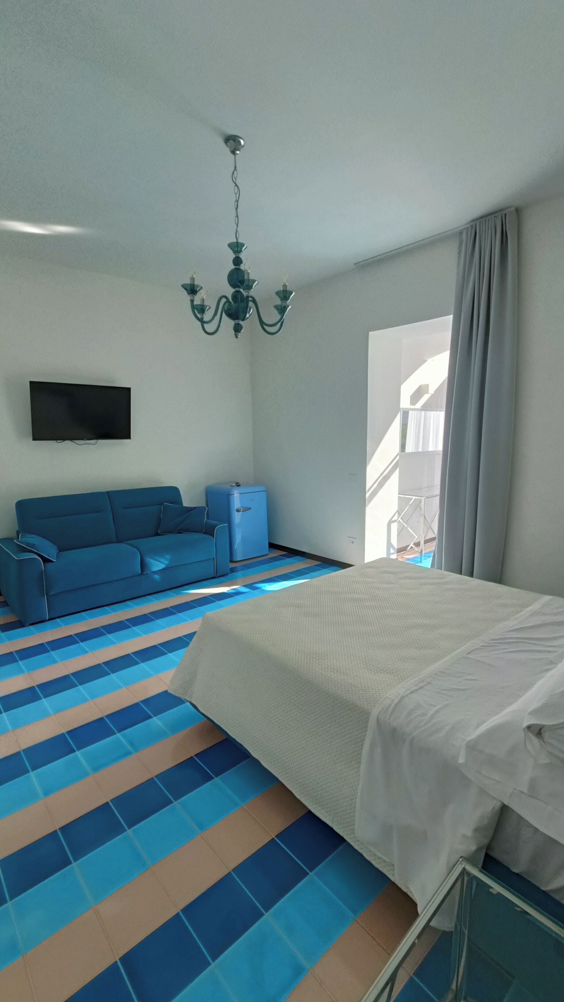 A hotel room with a bed, a blue sofa, a small table, a TV, and a window with curtains.