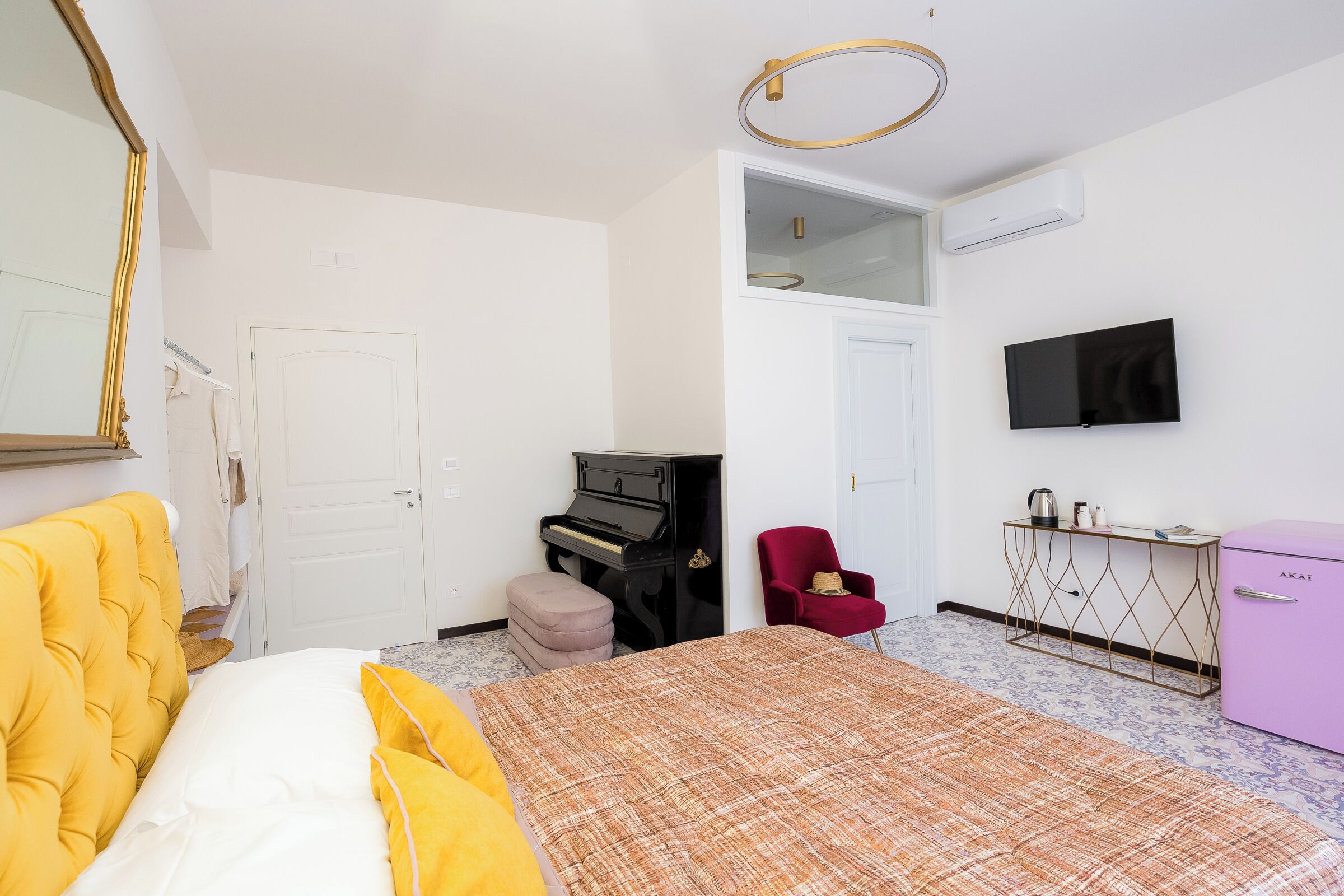 A bedroom with a bed, a piano, a red chair, a TV, and a minibar.
