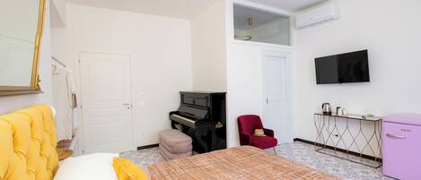 A bedroom with a bed, a piano, a red chair, a TV, and a minibar.