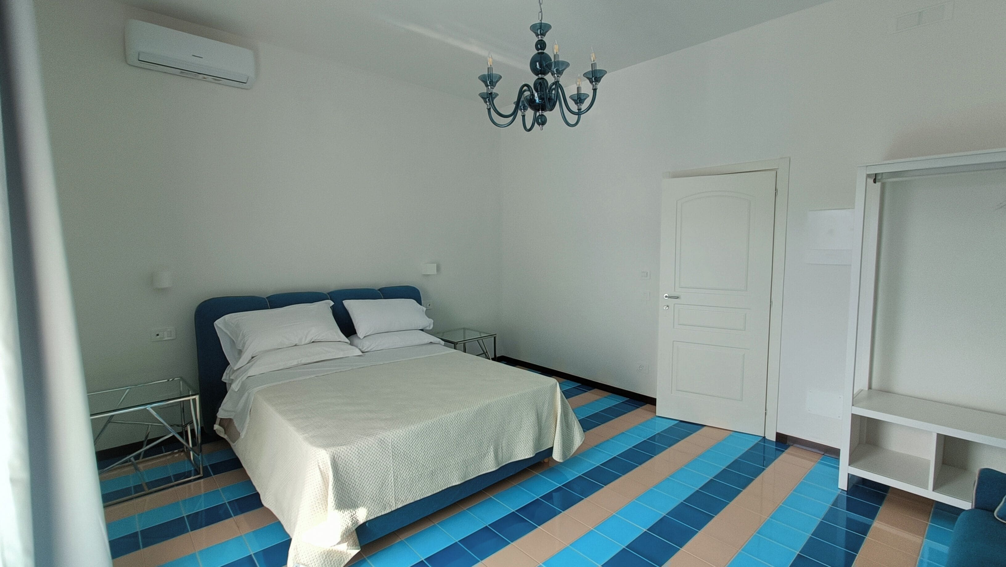 Quarto com cama, armário, lustre, radiador e piso ladrilhado.