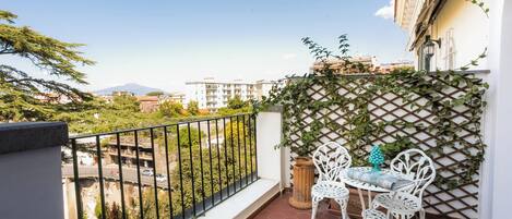 A balcony with a view of a cityscape, a white metal table with chairs, and a wooden planter.