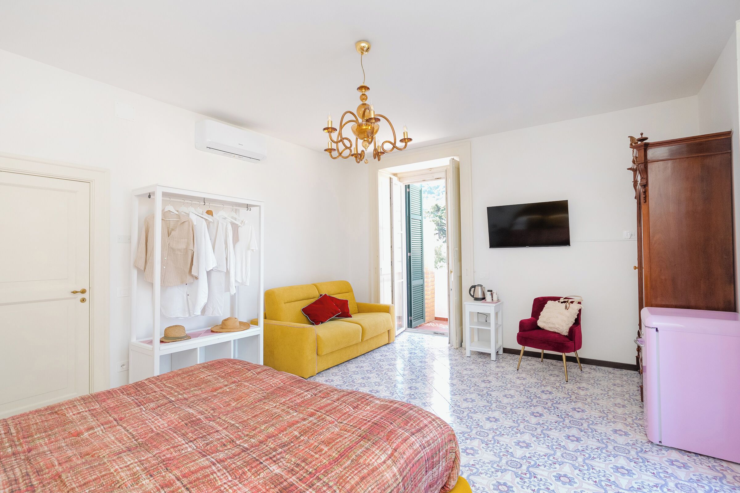 Um quarto com cama, um sofá amarelo, uma poltrona vermelha, uma televisão e um guarda-roupa.