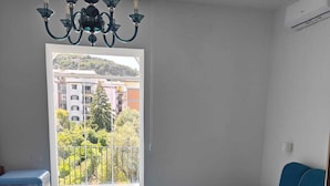 Un dormitorio con cama, cómoda, lámpara de araña y vista a un balcón con suelo de baldosas.