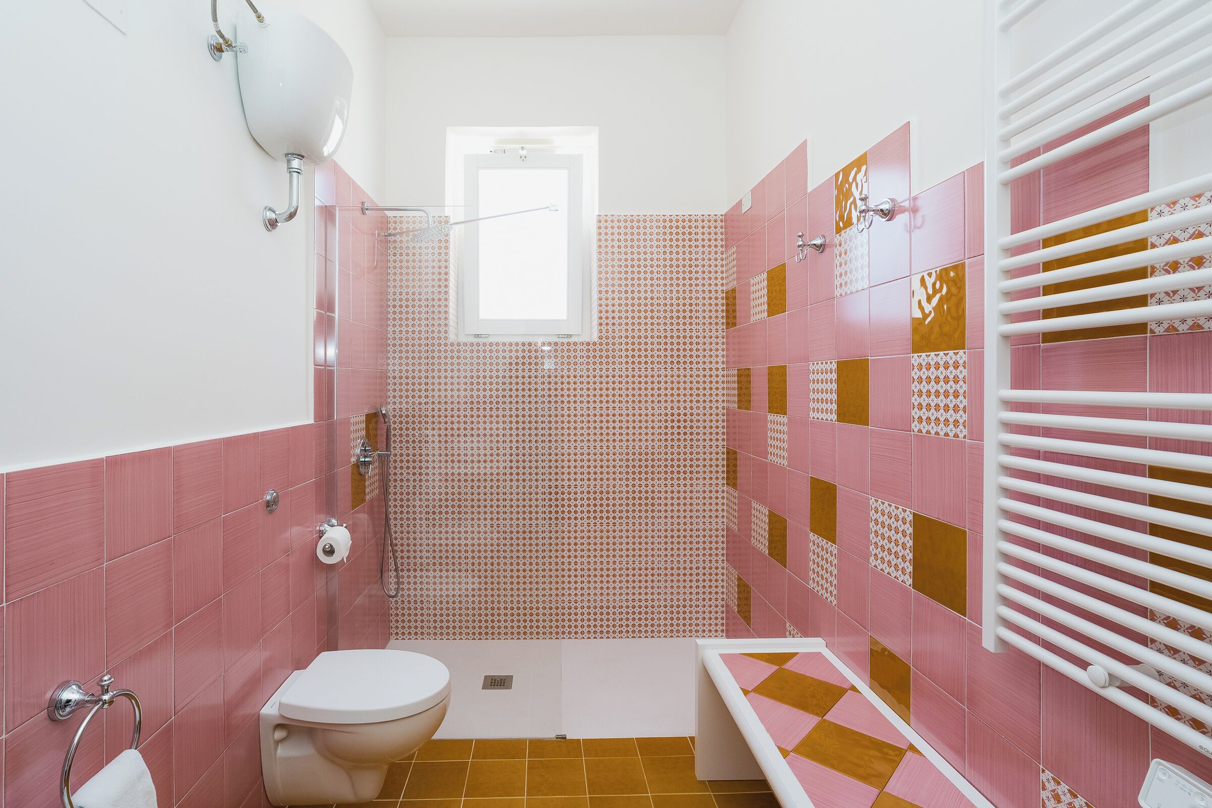 A bathroom with pink and white tiles, a toilet, a sink, and a shower area.