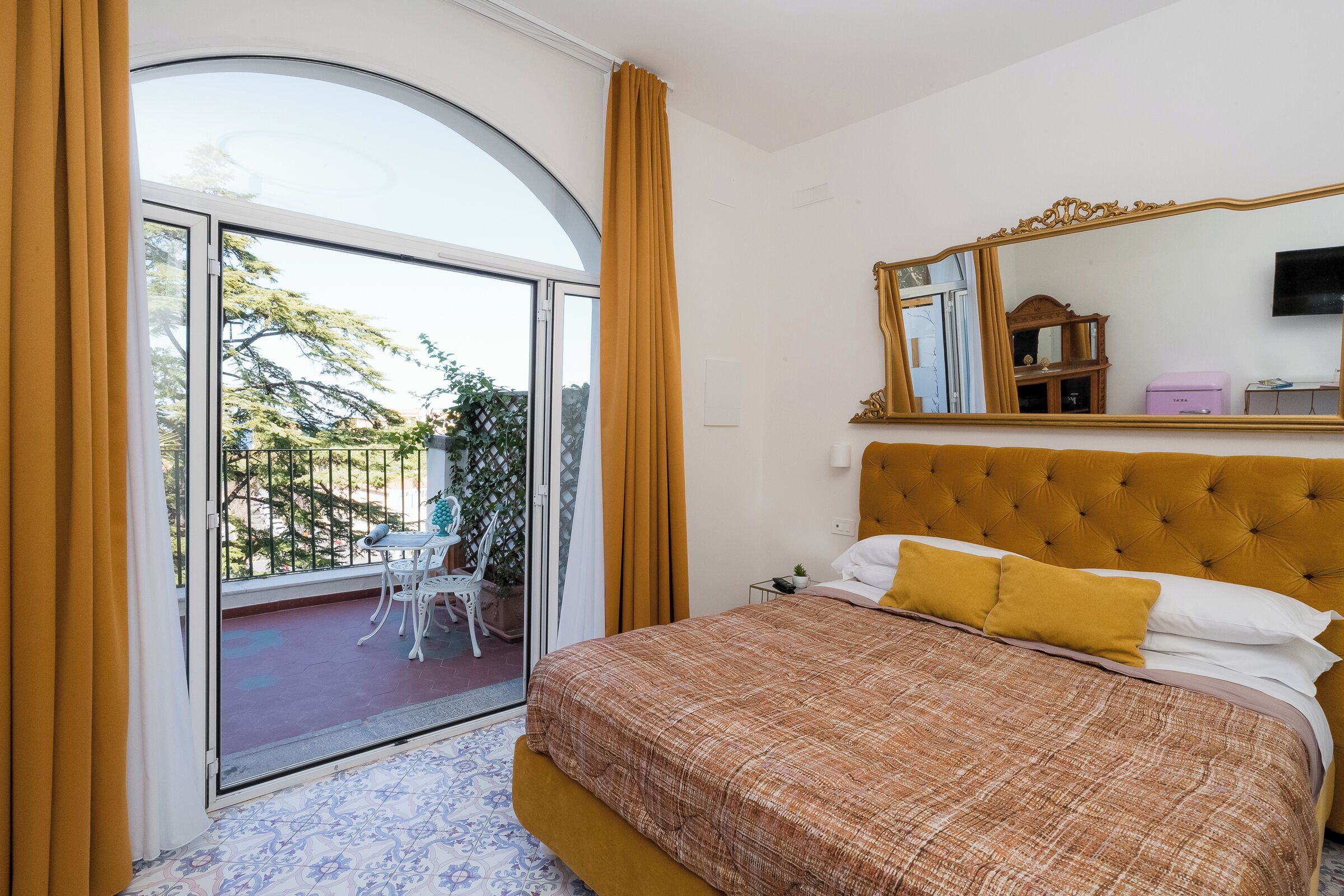 A bedroom with a large bed, a sliding glass door to a balcony, and a mirror on the wall.