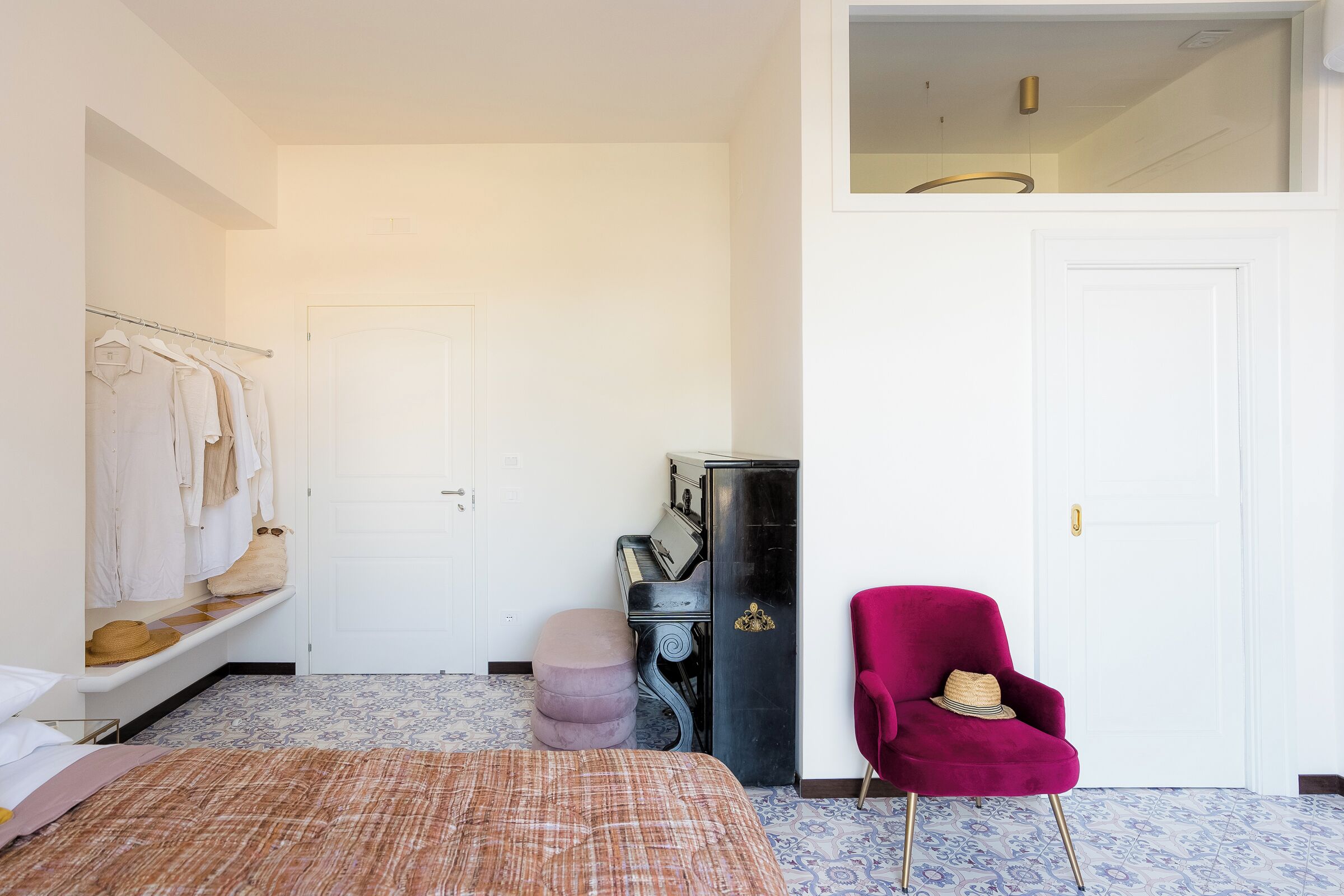 A bedroom with a bed, a wardrobe, a piano, a red chair, and a small stool.