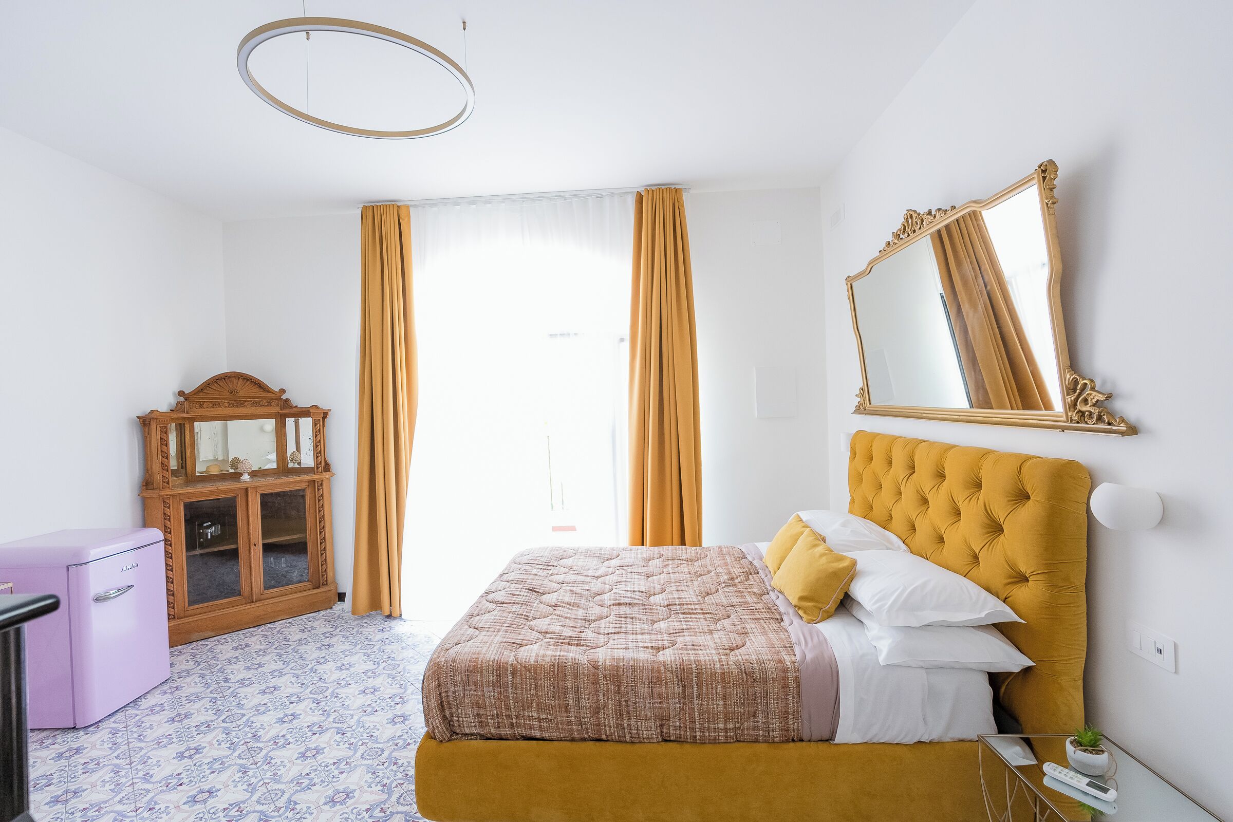 Een slaapkamer met een bed, een dressoir, een spiegel en een raam met gordijnen.
