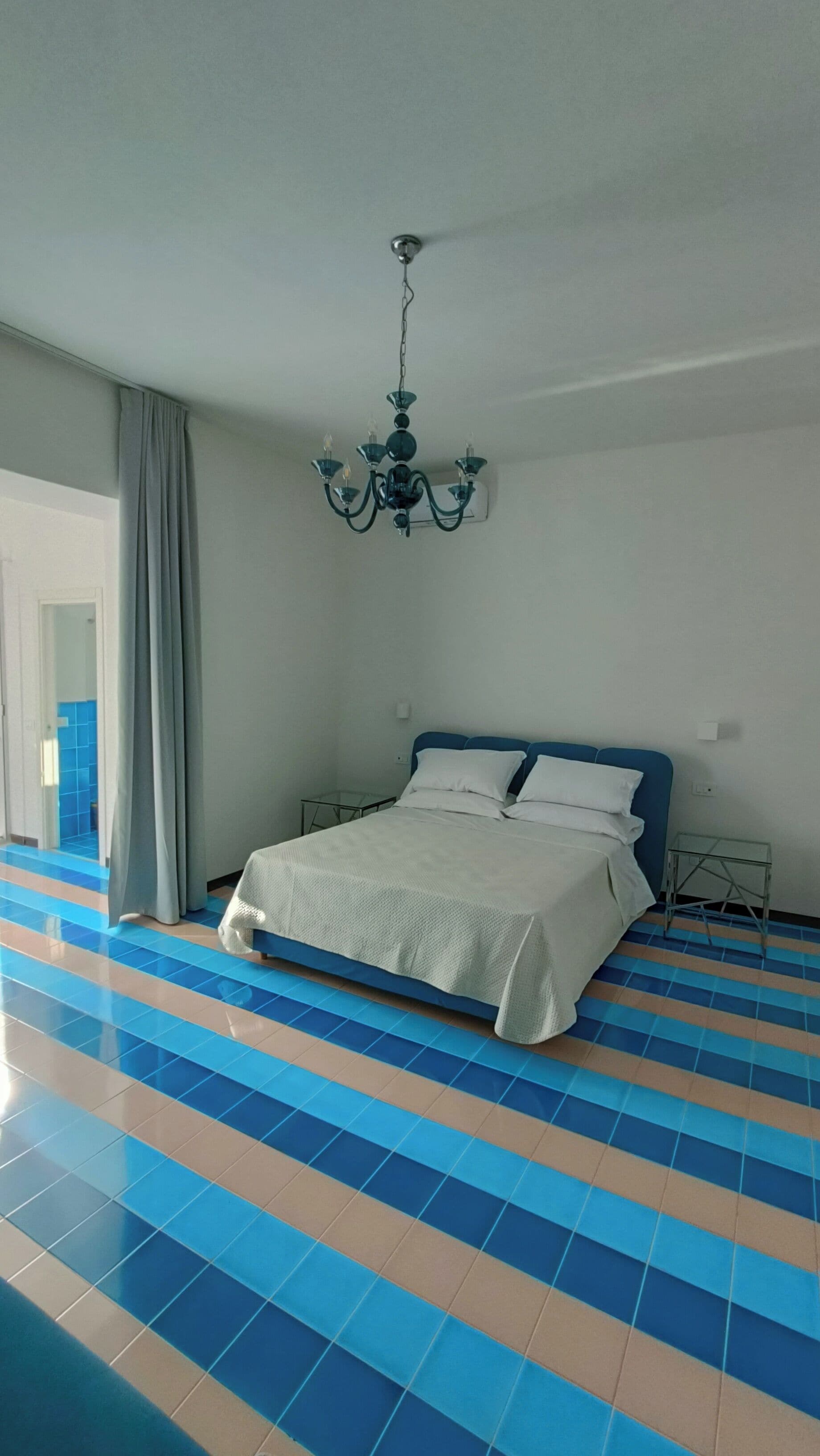 Ein Schlafzimmer mit einem Bett, einer Chandelierleuchtre und einem blau-beigen Fliesenboden.