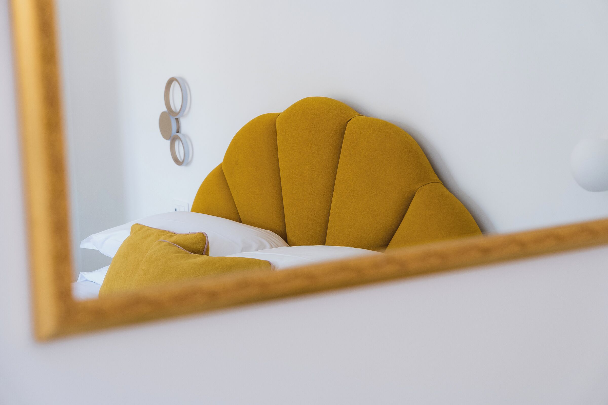 A bed with a mustard-colored headboard and white bedding.