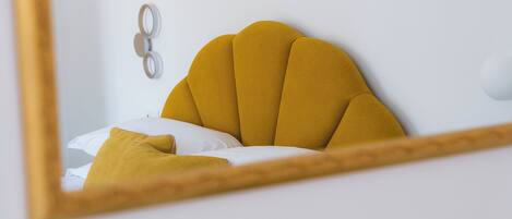 A bed with a mustard-colored headboard and white bedding.