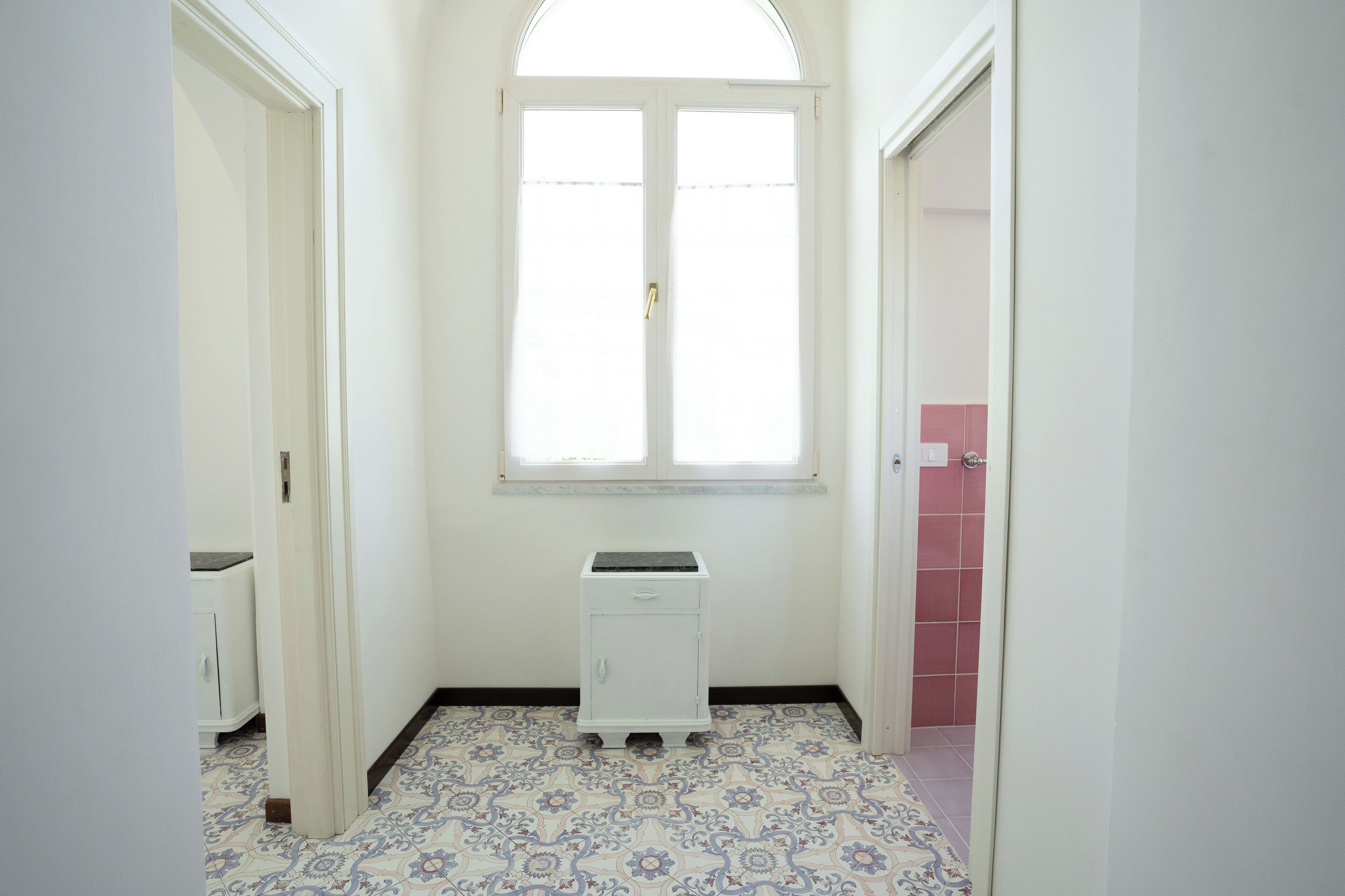 A narrow hallway with a patterned floor, a small white cabinet, and a window with a door.