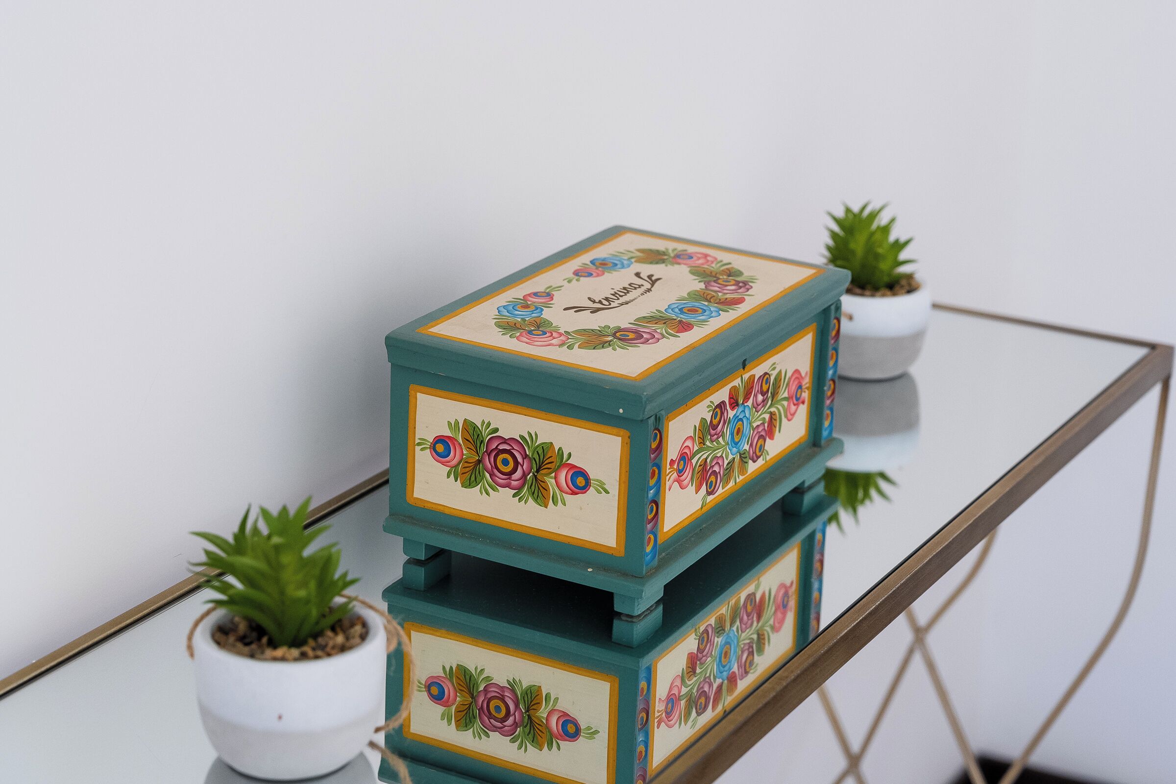 A glass table with teal-colored decorative boxes featuring floral patterns and the word "loving" on them.