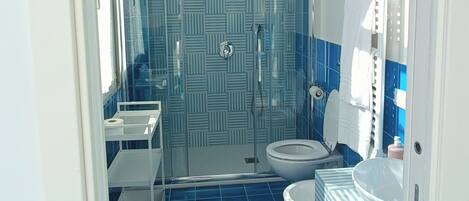 Un baño con azulejos azules, una ducha, un inodoro y un lavamanos.