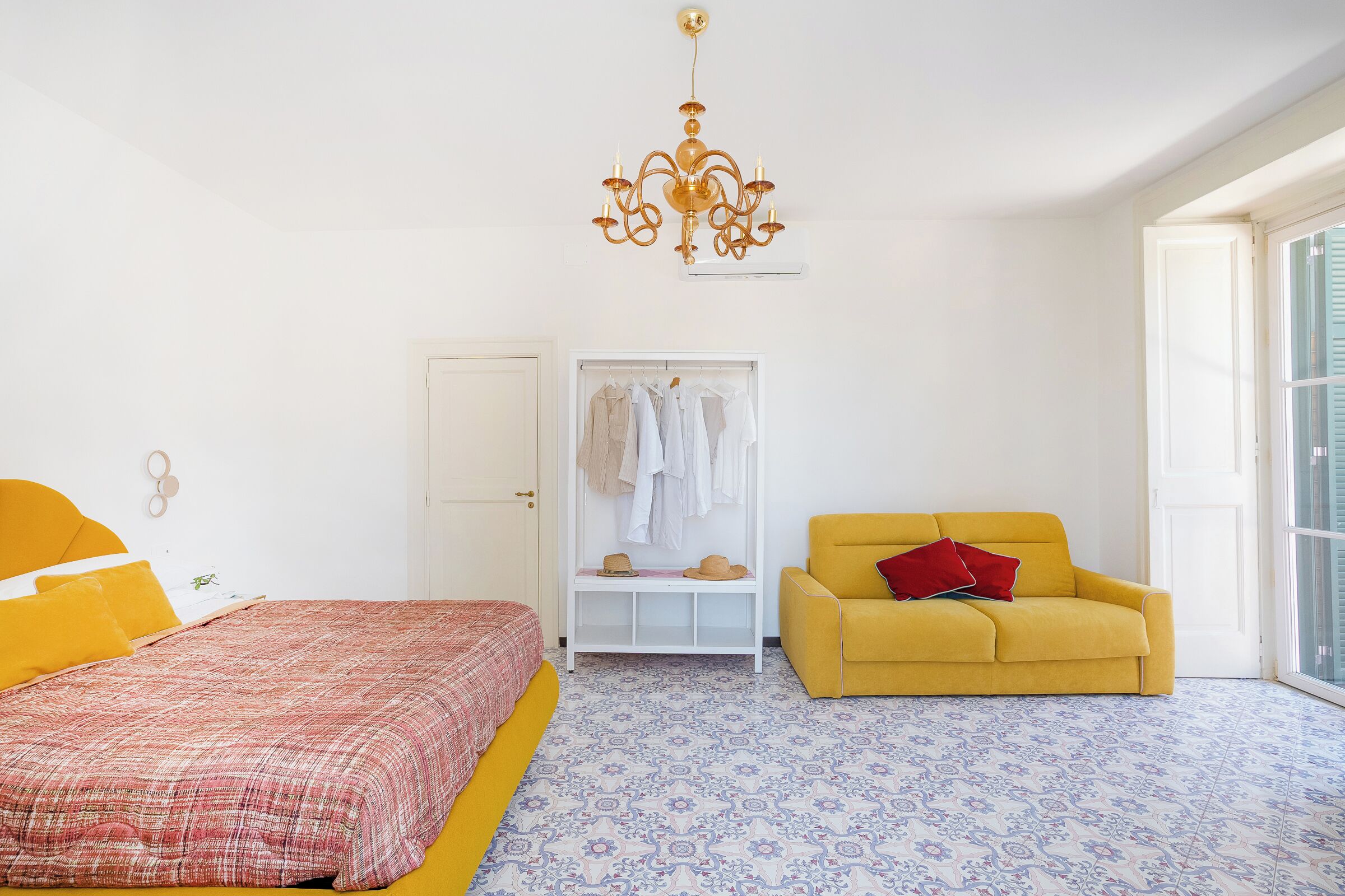 Une chambre à coucher avec un lit, un fauteuil jaune, une armoire et un lustre.