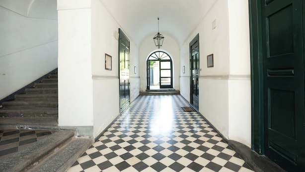 Un pasillo con piso a cuadros, paredes blancas y una puerta verde al final.