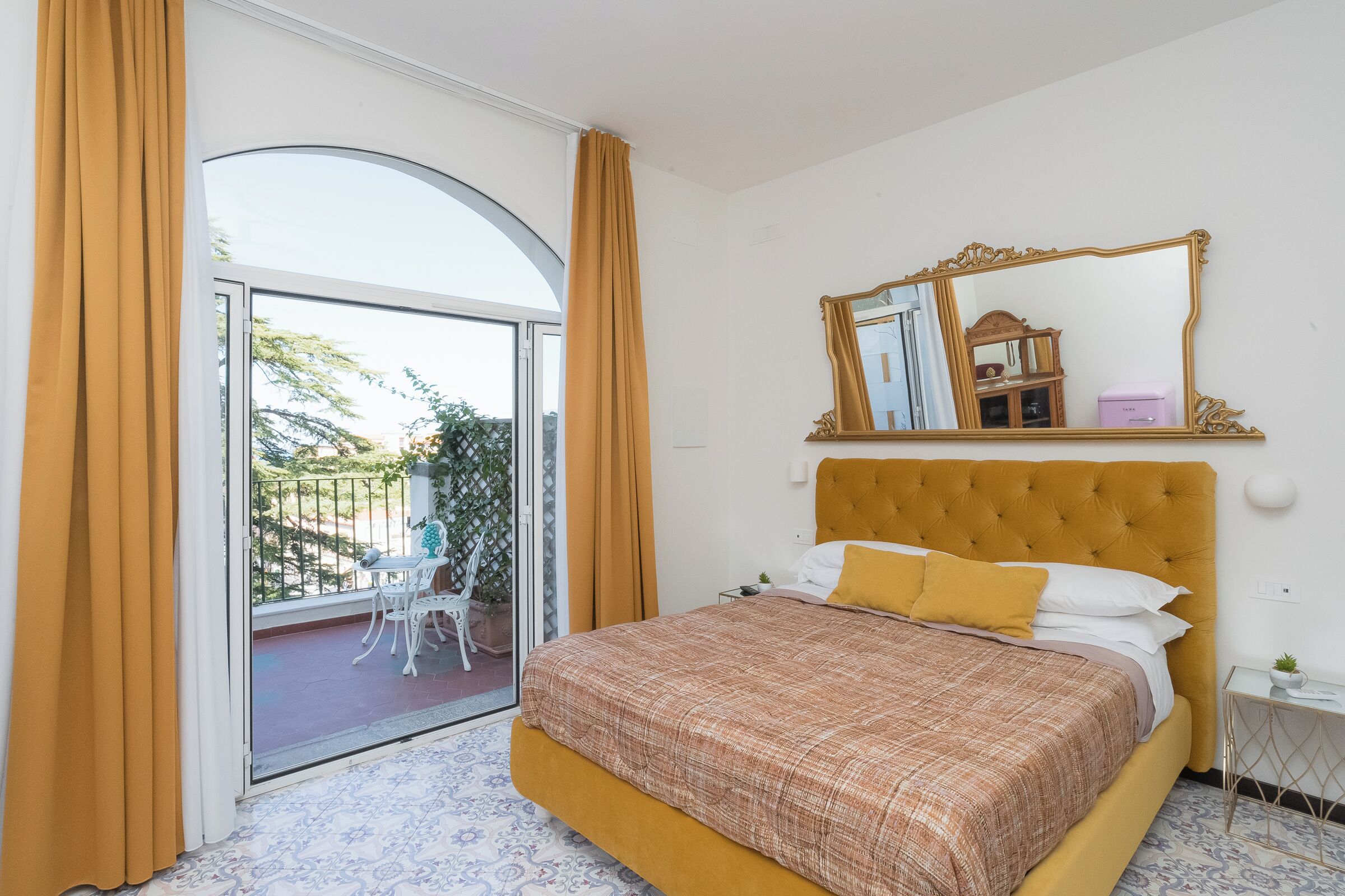Een slaapkamer met een groot bed, een schuifdeur naar een balkon en een spiegel boven het bed.