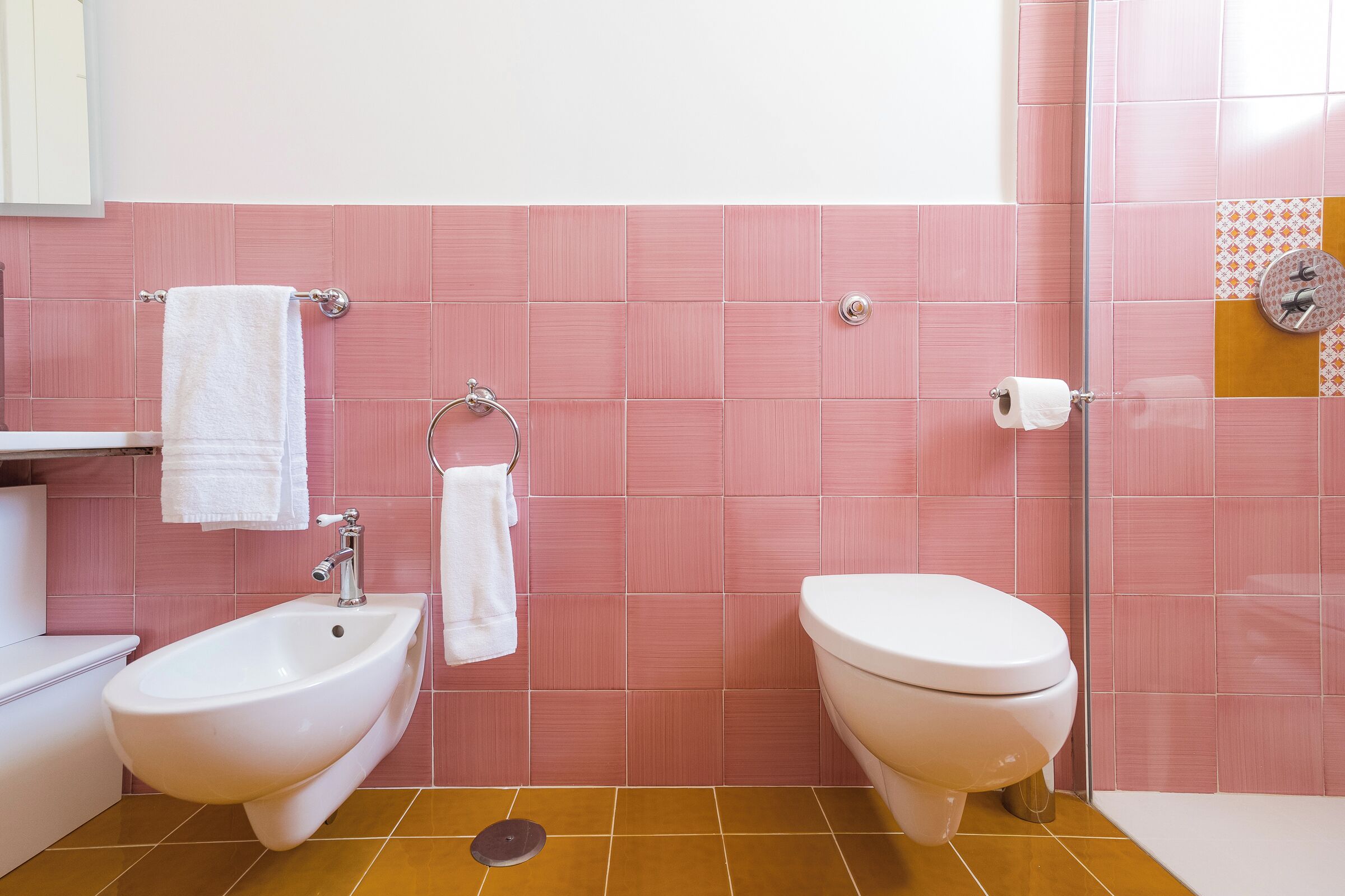 Un baño con azulejos rosas, un bidé, un inodoro y una zona de ducha.