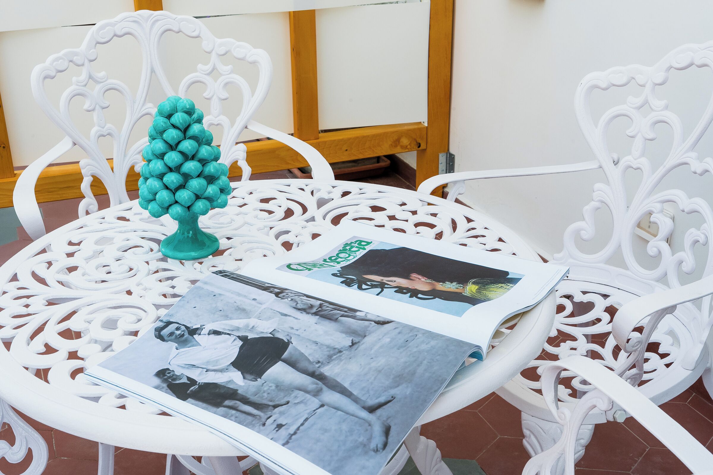 A white metal table with a decorative tree, a magazine, and a photograph.