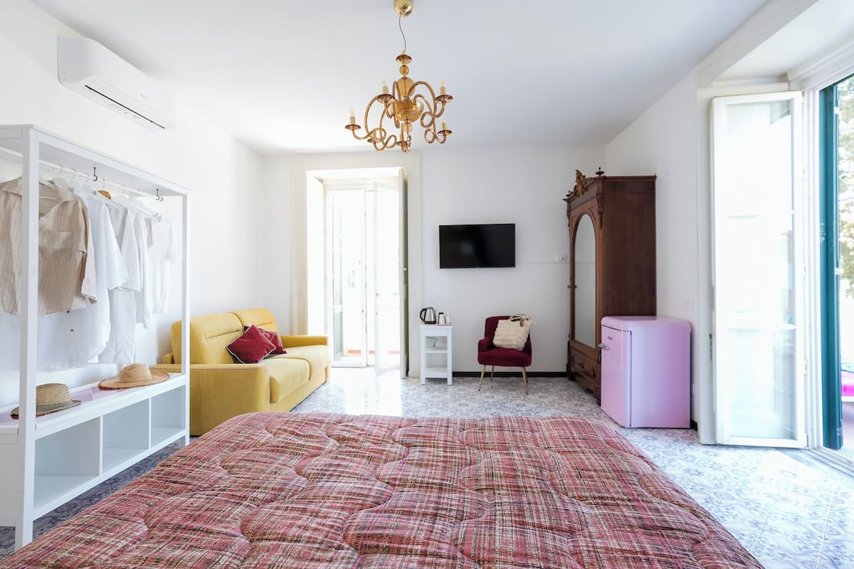 A bedroom with a bed, a wardrobe, a television, a small table, a chair, and a pink refrigerator.