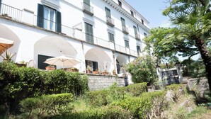 Un edificio blanco con varios balcones y ventanas arqueadas. Se ven plantas en macetas y muebles de exterior.
