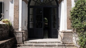 Entrada de un edificio con un camino de piedra que lleva a una puerta negra, flanqueada por paredes blancas y un pequeño balcón.