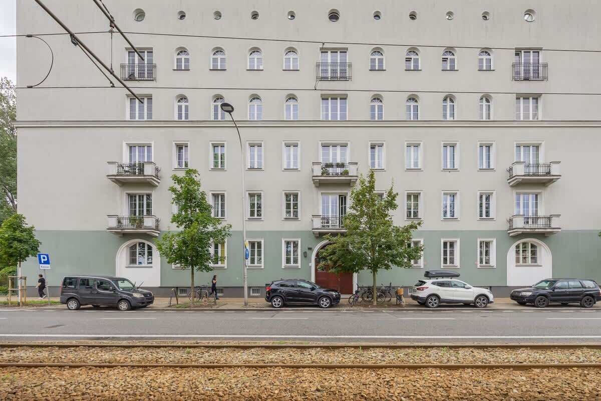A multi-story building with a row of balconies, a parking sign, and a railway track in the foreground.