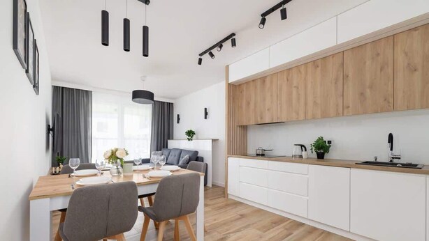 Una cocina moderna con armarios blancos, encimeras de madera y una zona de comedor con mesa y sillas de madera.