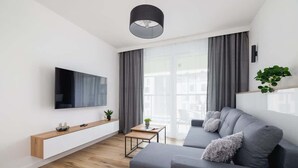 Una sala de estar moderna con un televisor de pantalla plana, un sofá gris, un mueble bajo de madera y una mesita con una planta.